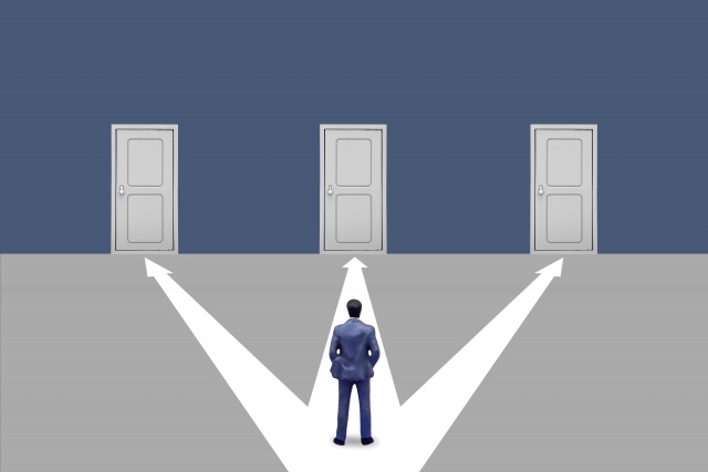 営業転職で複数の選択肢を前に、どれを選ぶか迷って立ち止まる男性のイメージ