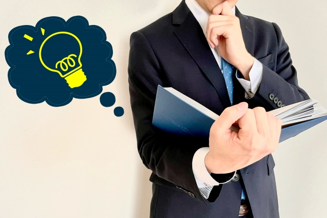 スーツ姿の男性が本を持ち考えている様子と電球アイコン(営業の環境を冷静に判断するイメージ)