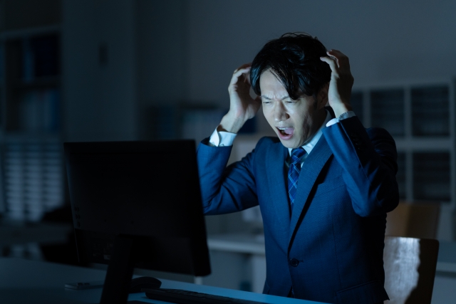 残業で疲れてパソコンの前で頭を抱える営業マンのイメージ