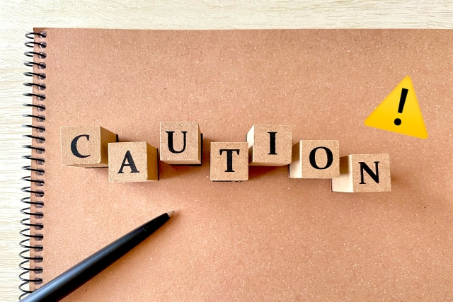 CAUTIONの文字ブロックと注意マークが置かれたノートのイメージ画像