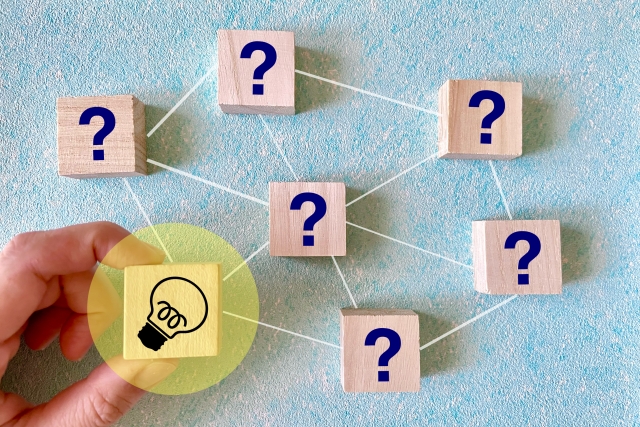 複数の疑問をつなぐ図の中で、ひらめきを示す電球マークのブロックを手で持っている画像
