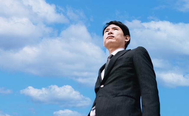 青空を見上げるスーツ姿の男性