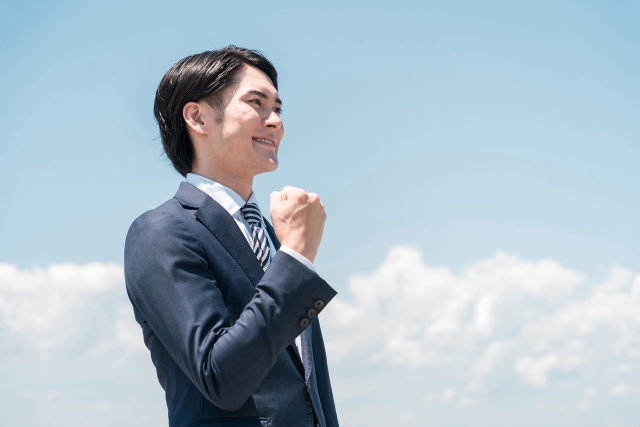 青空の下で拳を握るスーツ姿の男性