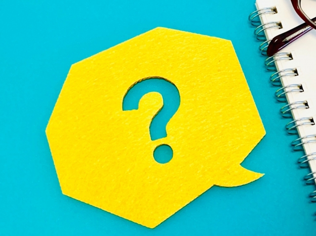 青い背景の上に置かれた、黄色の吹き出し型メモとクエスチョンマーク