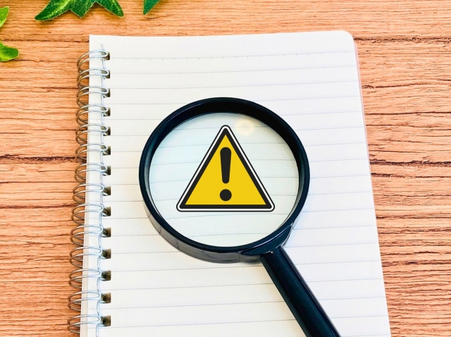 虫眼鏡で警告マークを拡大して確認しているノートのイメージ