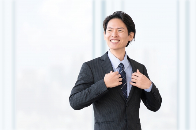 スーツ姿でネクタイを整えながら前向きな表情を見せる若い男性会社員