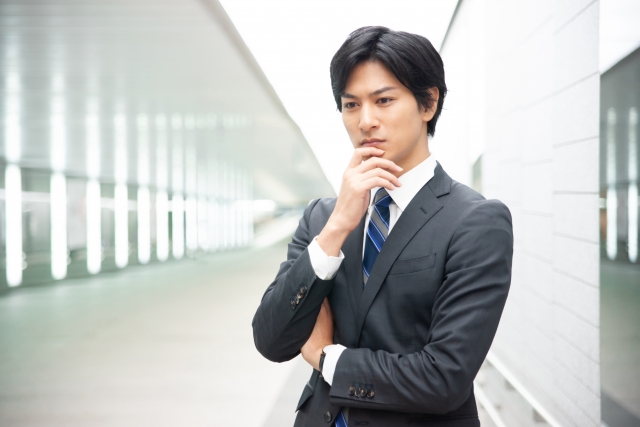 スーツ姿の男性が通路で考え込んでいる様子を写したイメージ画像