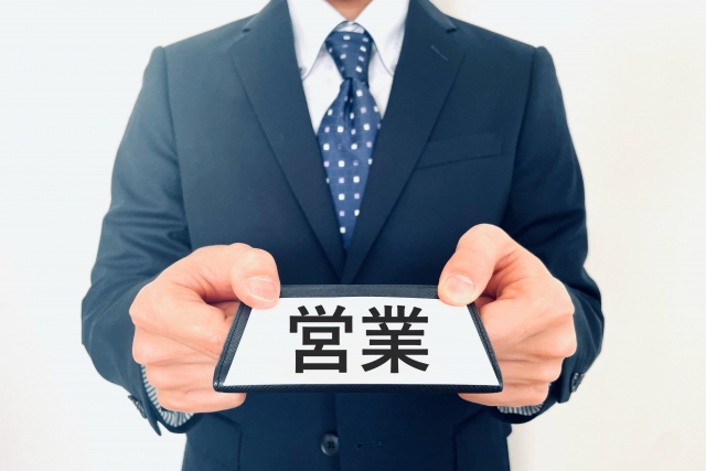 営業職を表す名刺を持つスーツ姿の男性