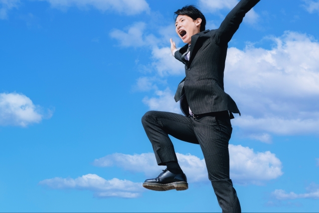 青空の下でジャンプするスーツ姿の男性
