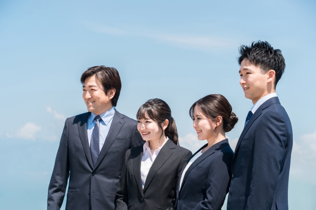 青空の下でスーツ姿の若手社会人が並ぶ画像。営業未経験から正社員就職を目指す人の前向きな未来を表している。