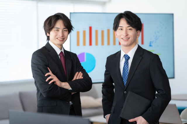 スーツ姿の男性2人がオフィスで立っている画像。営業職に特化した転職支援を受けるイメージ。