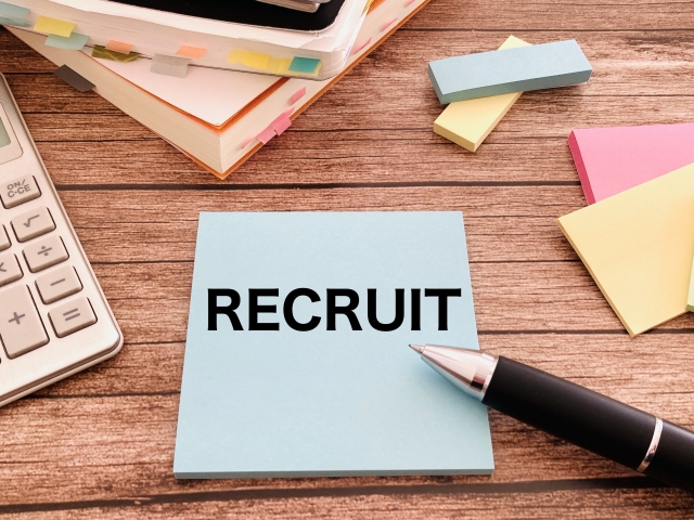 RECRUITと書かれた付箋とペン、電卓、書類が置かれた採用・転職活動のイメージ画像