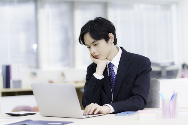 ノートパソコンを見ながら営業職のストレスについて考えるスーツ姿の男性